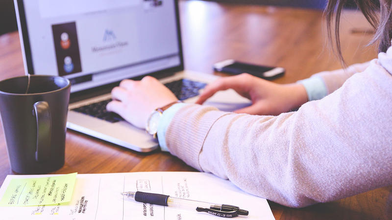 Woman working on laptop with paper work and cup of tea to the left of laptop